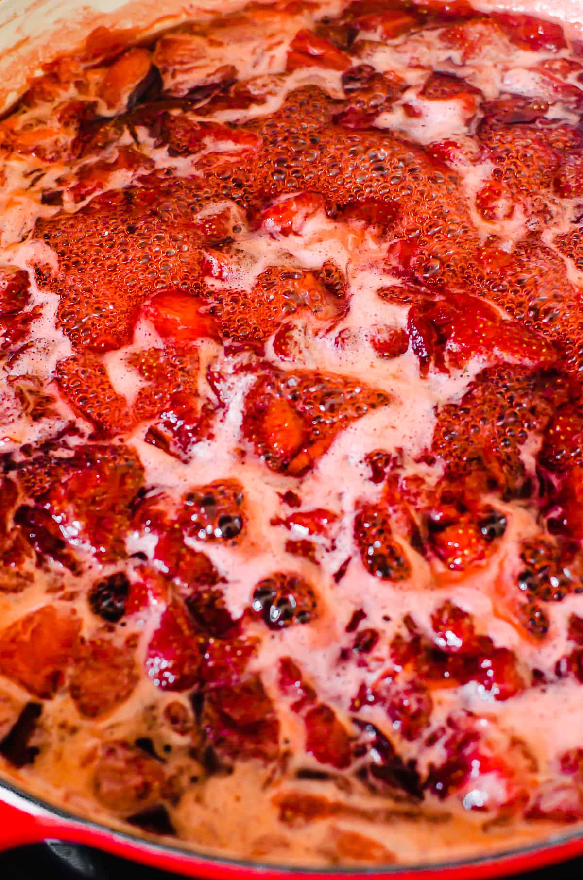 Foam forming on top of a pot of simmering strawberry jam.