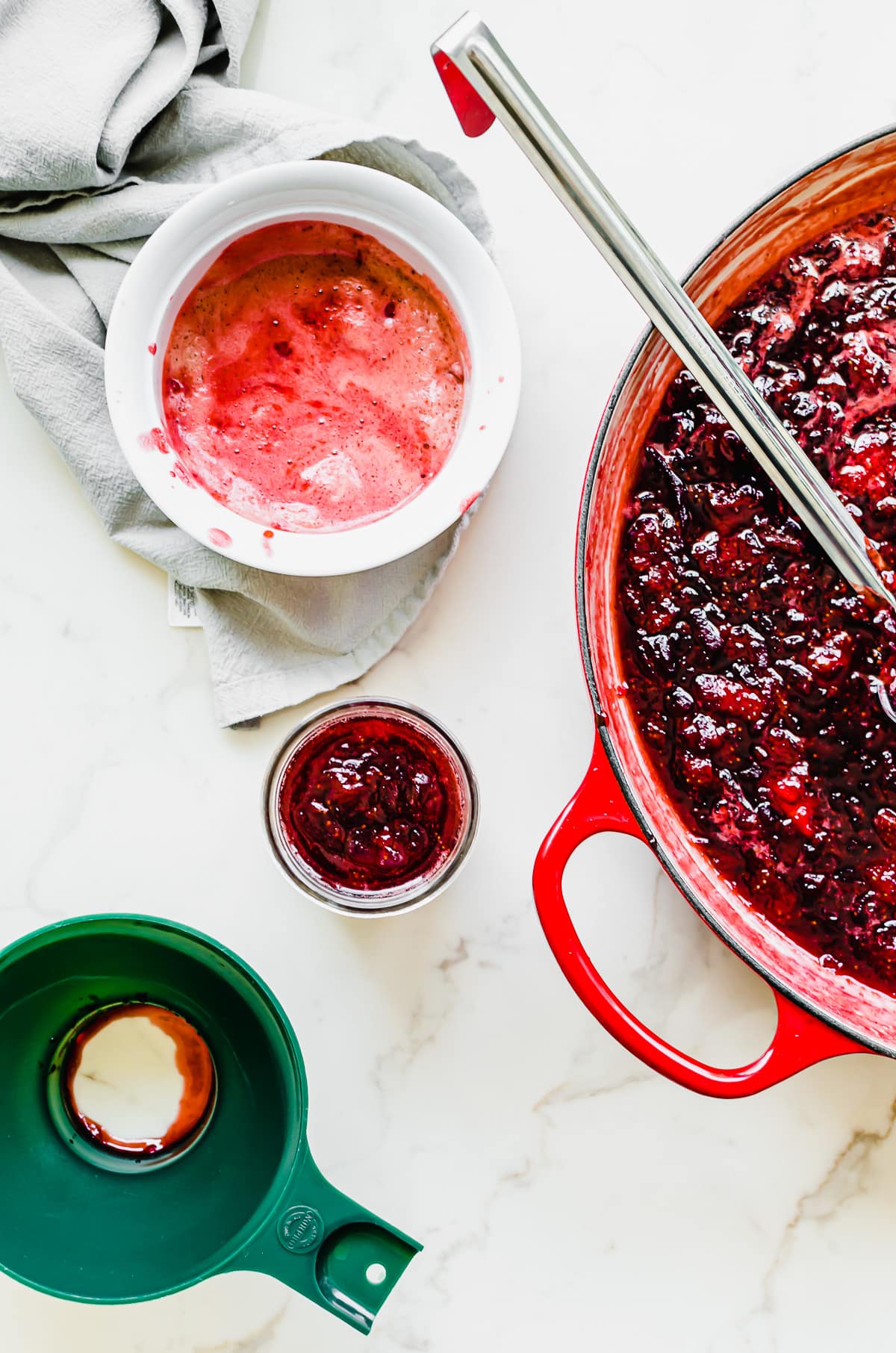 A large pot with strawberry jam and a ladle with a jam jar and funnel on the side.