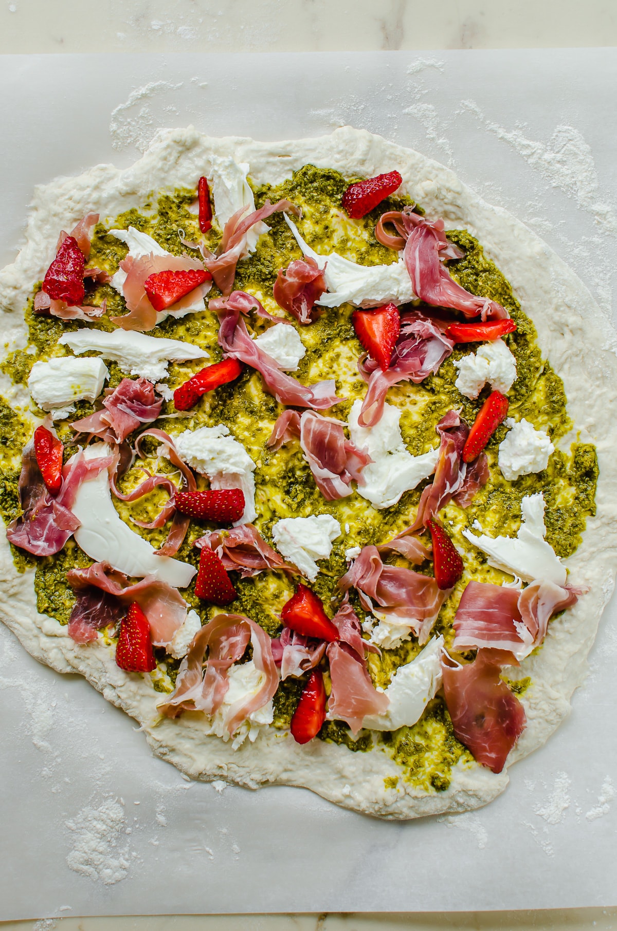 Pizza dough topped with pesto, fresh mozzarella, prosciutto and strawberries.