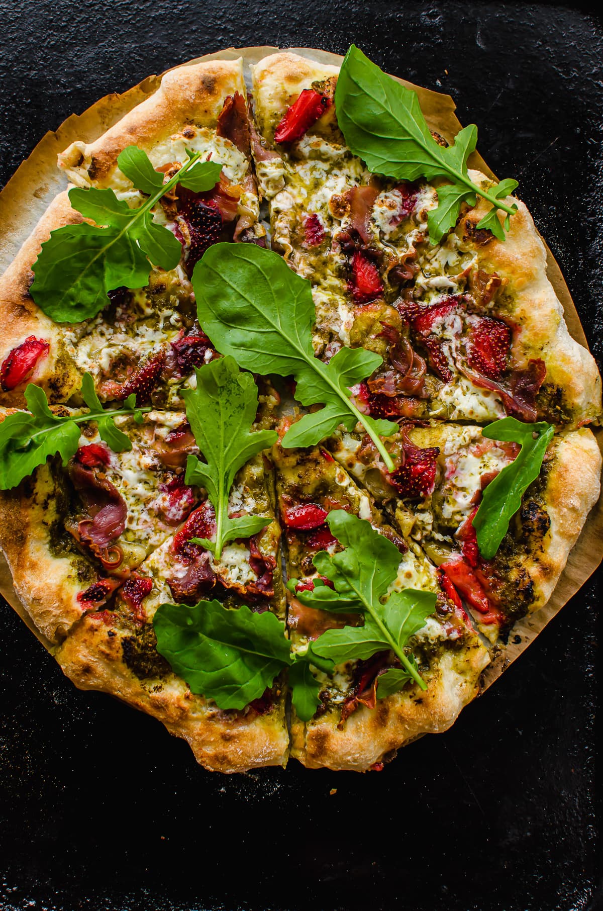 An overhead shot of a baked prosciutto pizza with strawberries and arugula.