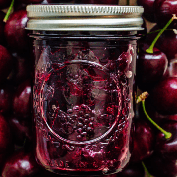 A jar of cherry jam surrounded by a background of cherries.