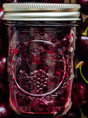 A jar of cherry jam surrounded by a background of cherries.