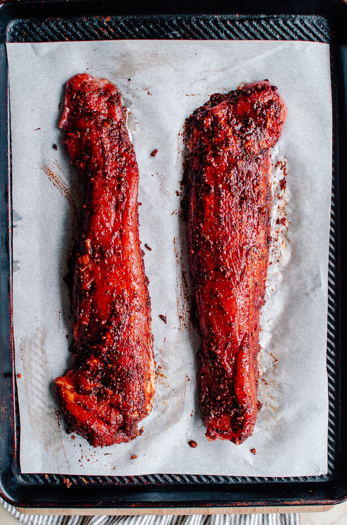 Two chile rubbed pork tenderloins on a baking sheet lined with parchment paper.
