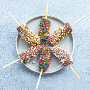 Chocolate-dipped frozen bananas on a blue plate.