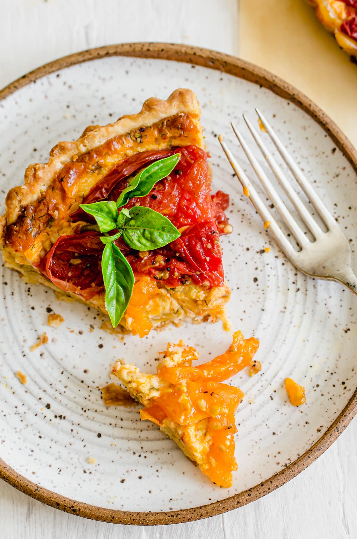 A slice of tomato tart on a plate with a fork and bite cut off. 