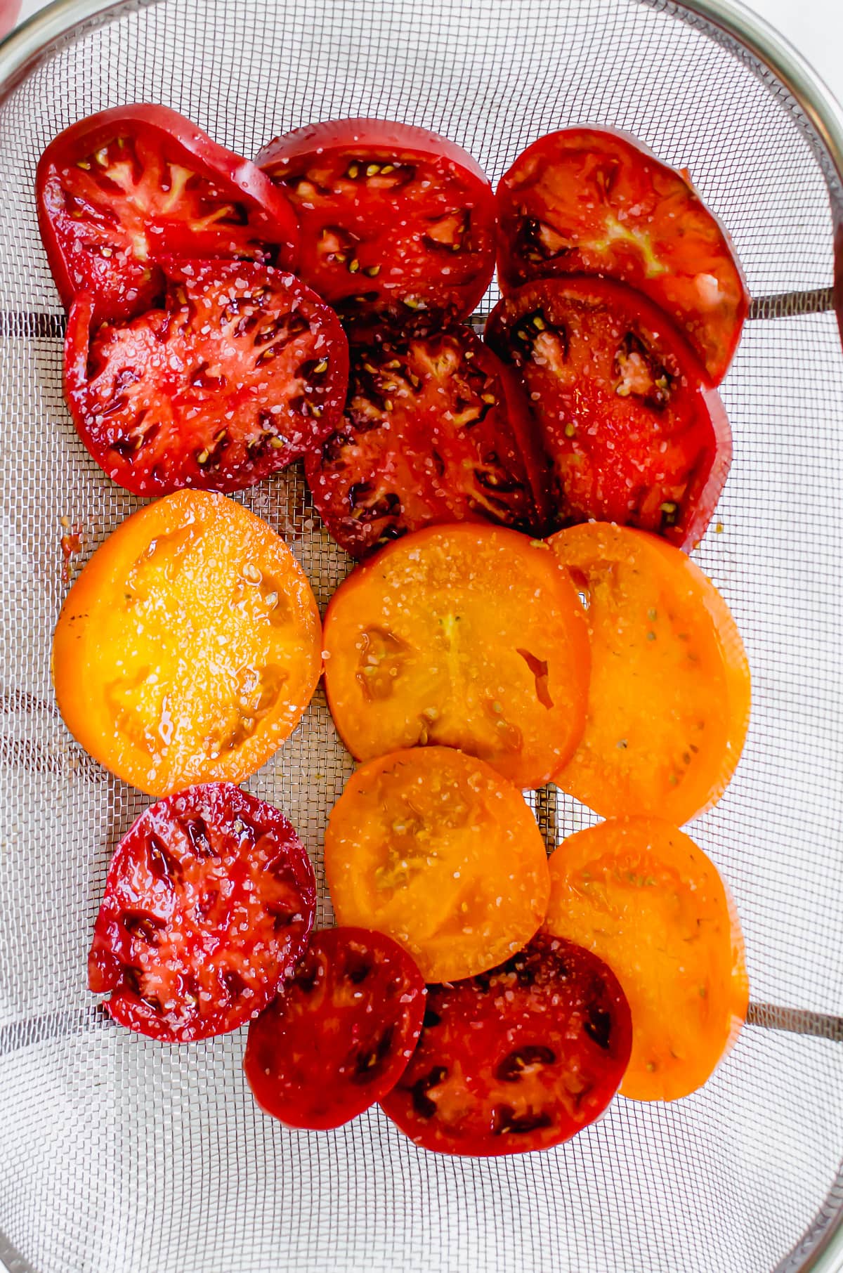 Tomato slices draining in a wire mesh colander. 