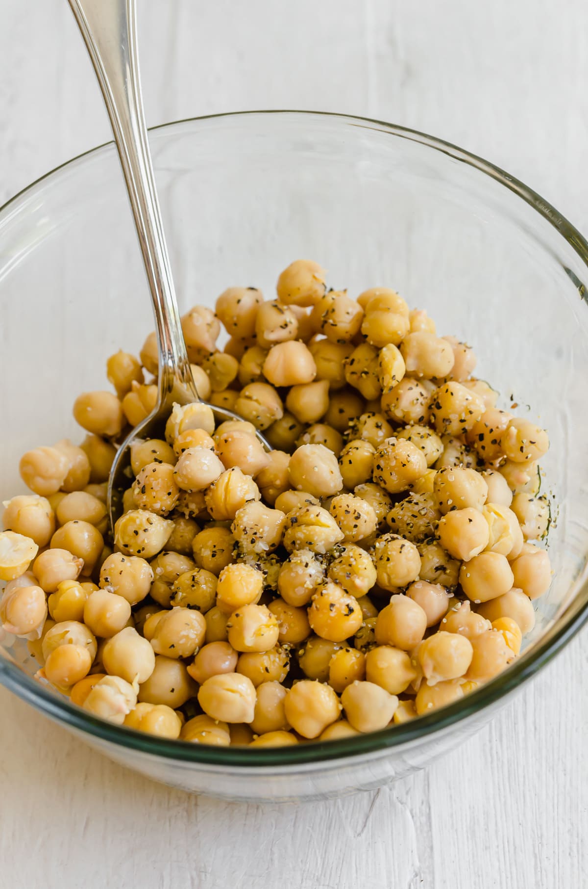 Chickpeas being tossed with oil and seasonings in a glass bowl.