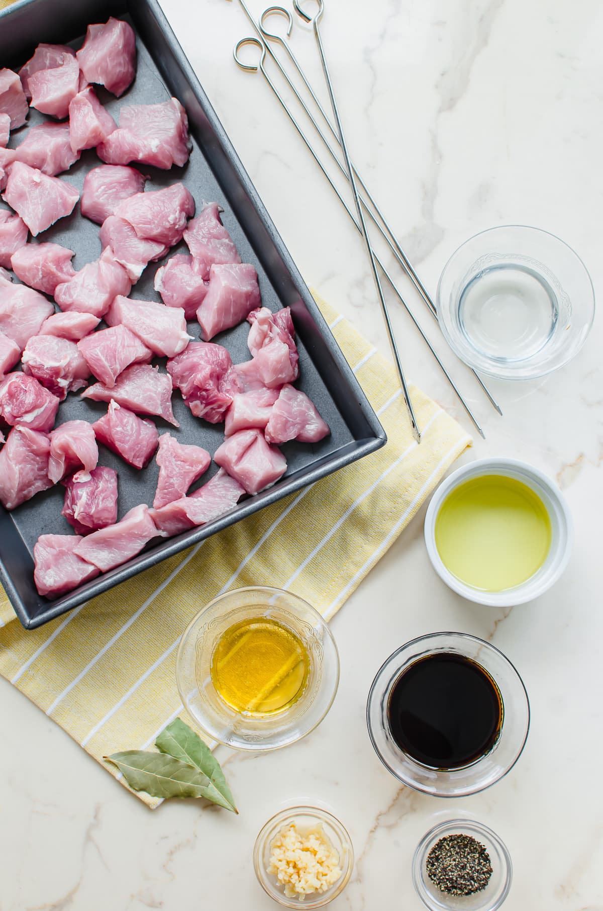 Pork tenderloin pieces in a pan with bowls for adobo marinade on the side.