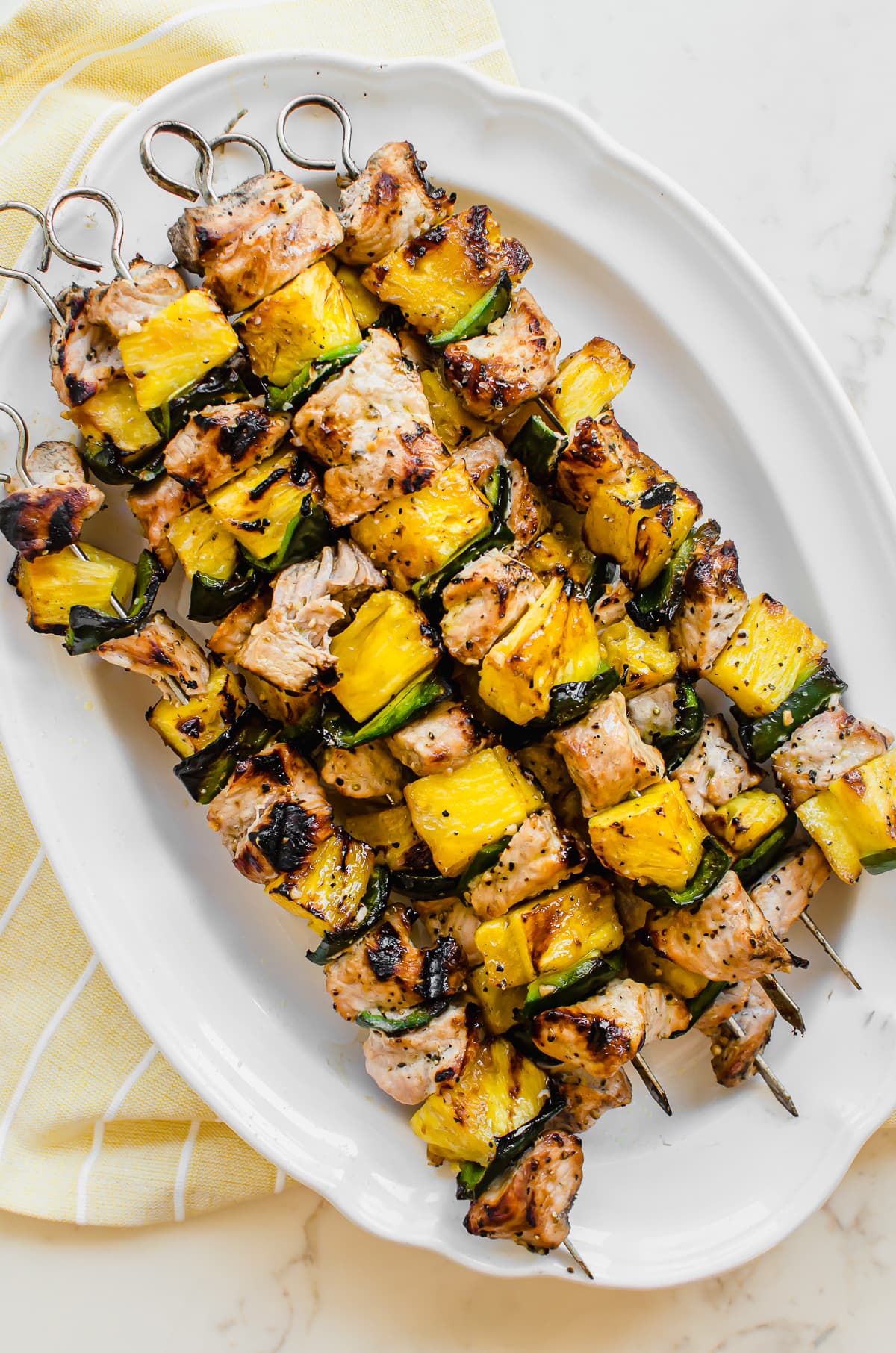A white platter on a yellow towel with pork pineapple kabobs.