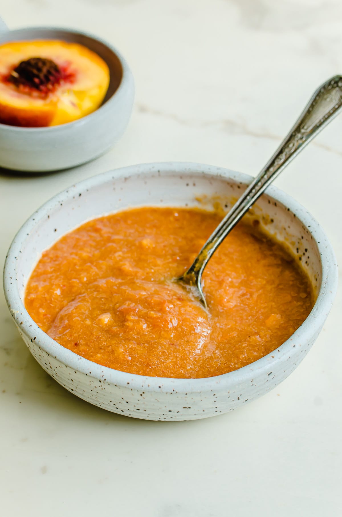 A ceramic speckled bowl filled with peach puree and an antique spoon.