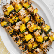 A white platter on a yellow towel with pork pineapple kabobs.
