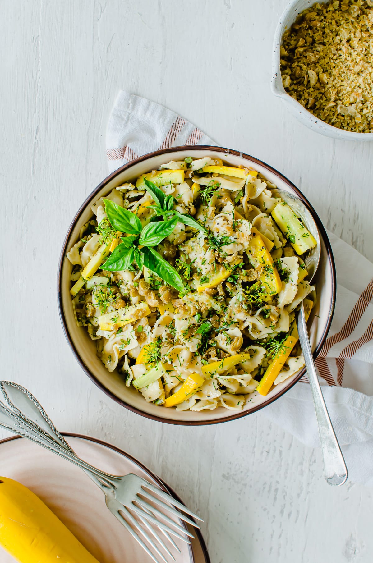 Overhead shot of a rimmed bowl with pasta salad and a bowl of chickpea breadcrumbs on the side.