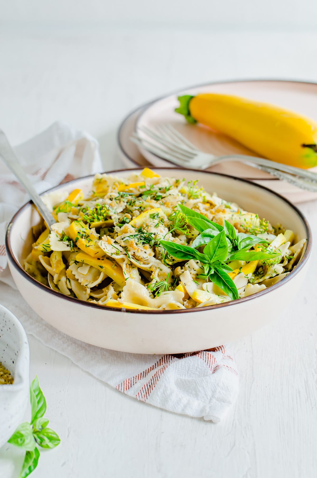 A side shot of a pink pasta bowl filled with summer pasta salad and garnished with basil.