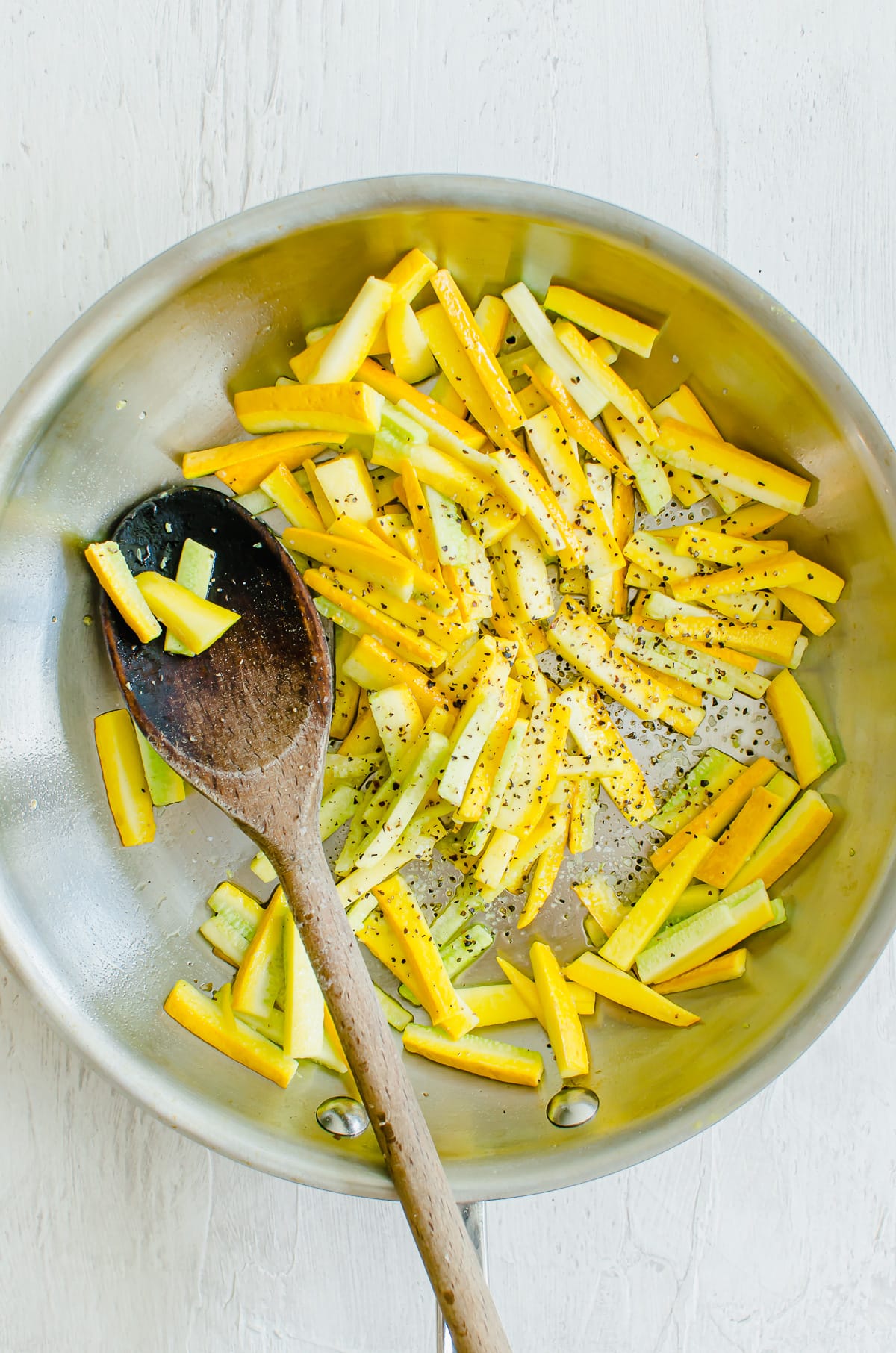 Yellow zucchini in a saute pan with a wooden spoon.