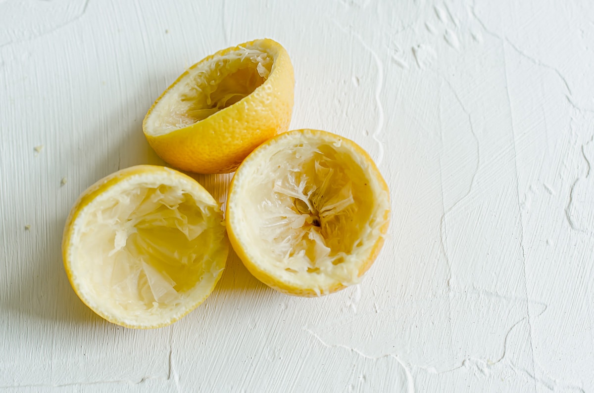 Three lemon halves with the pulp and juice removed on a white surface.