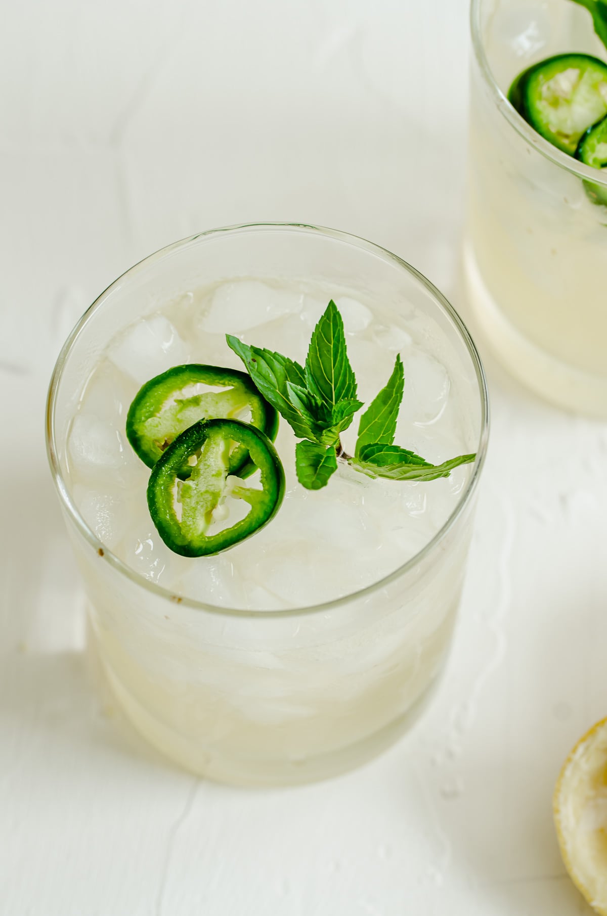 A glass of a lemon beverage garnished with jalapeño slices and a mint sprig.