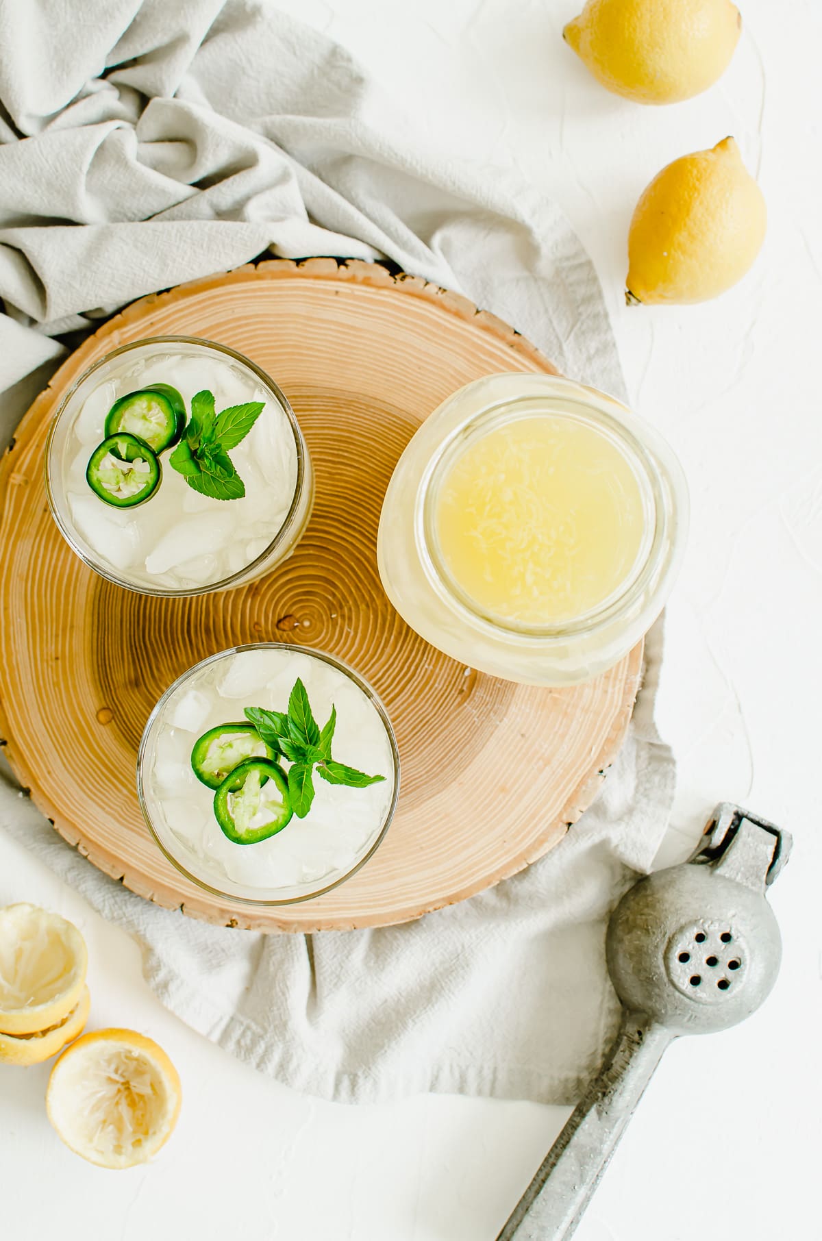 Two glasses of lemonade with a large jar of lemonade on a wooden tray.