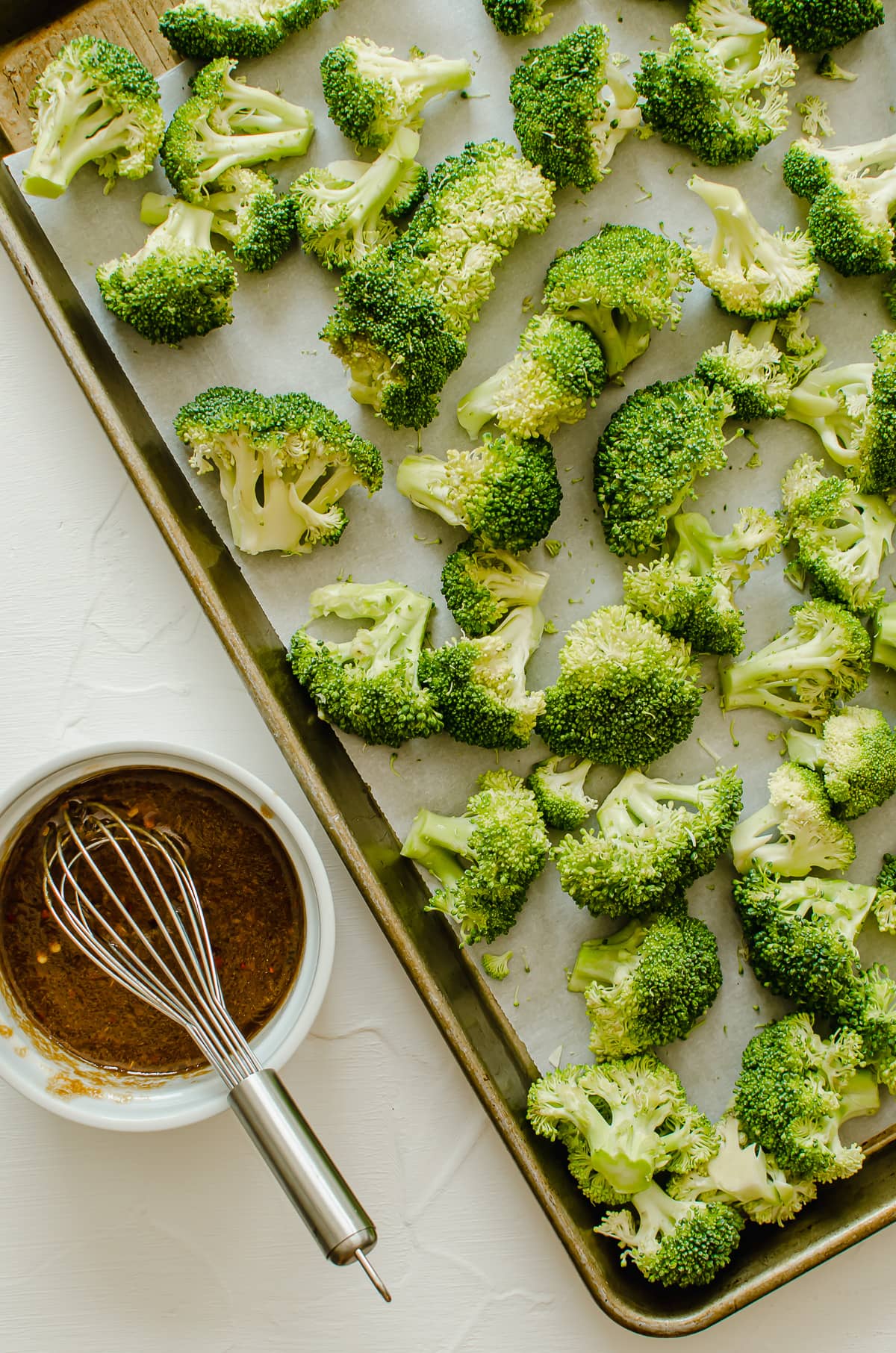 Raw broccoli florets on a sheet pan with a bowl of sesame sauce on the side.
