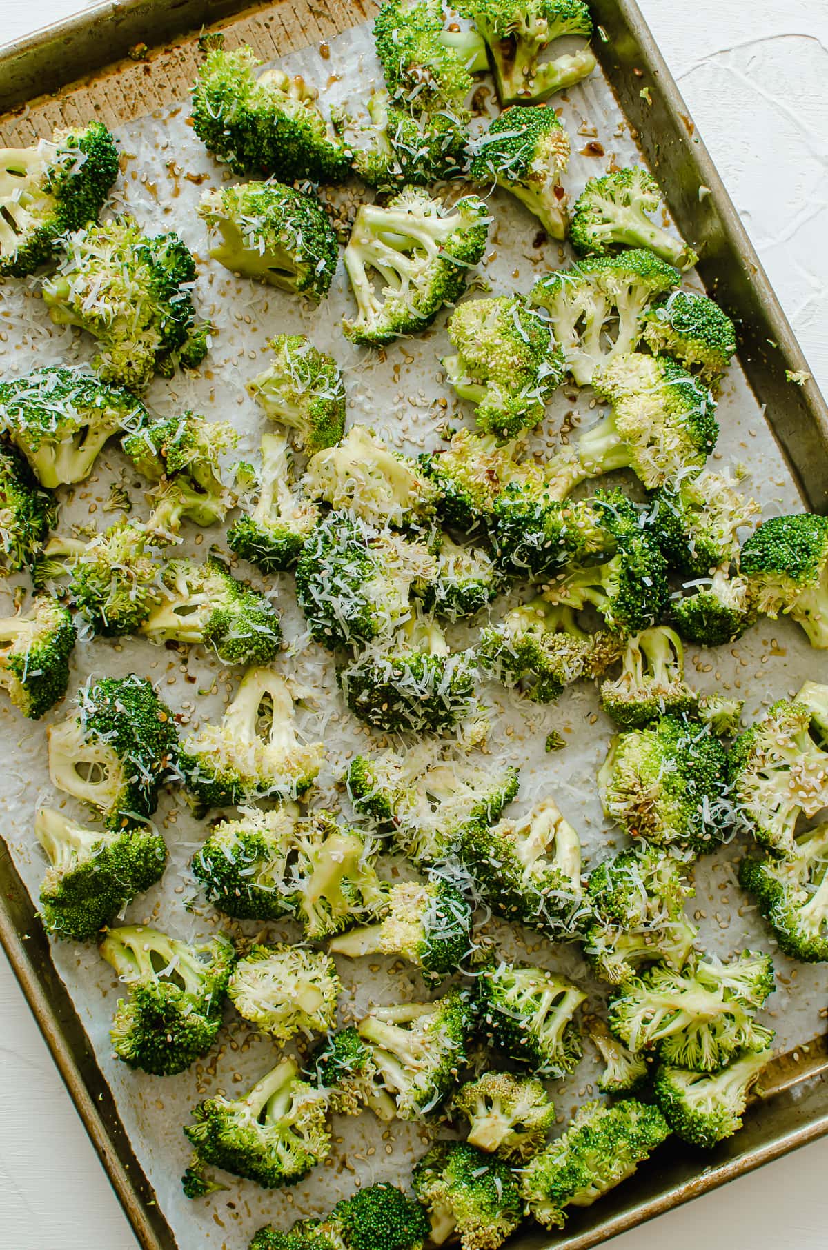 Uncooked broccoli on a sheet pan topped with Parmesan cheese.