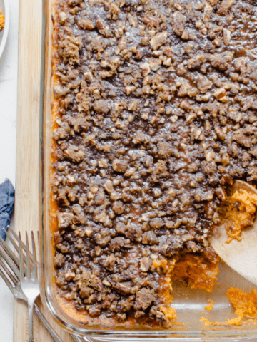 A large dish of sweet potato casserole with a spoon taking a serving out of the side.