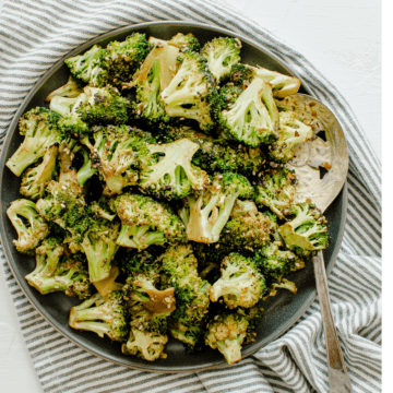 A square image with a gray plate of roasted broccoli.