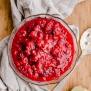 A glass bowl filled with apple cranberry sauce on a wood cutting board with a grey towel.