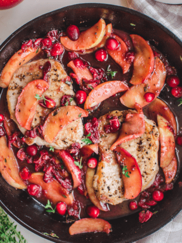 Pan-fried pork chops in a cast-iron skillet with a cranberry apple pan sauce.