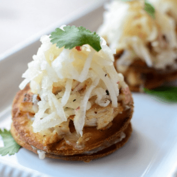 A side shot of a mini chicken tostada topped with apple slaw and a cilantro leaf.