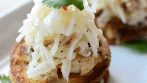 A side shot of a mini chicken tostada topped with apple slaw and a cilantro leaf.