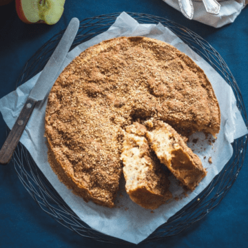 A cinnamon apple cake with two slices cut out on a piece of parchment paper with a navy blue background.