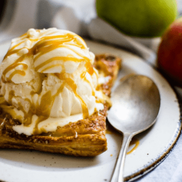 A side shot of an apple tart on a white plate topped with ice cream and caramel sauce.