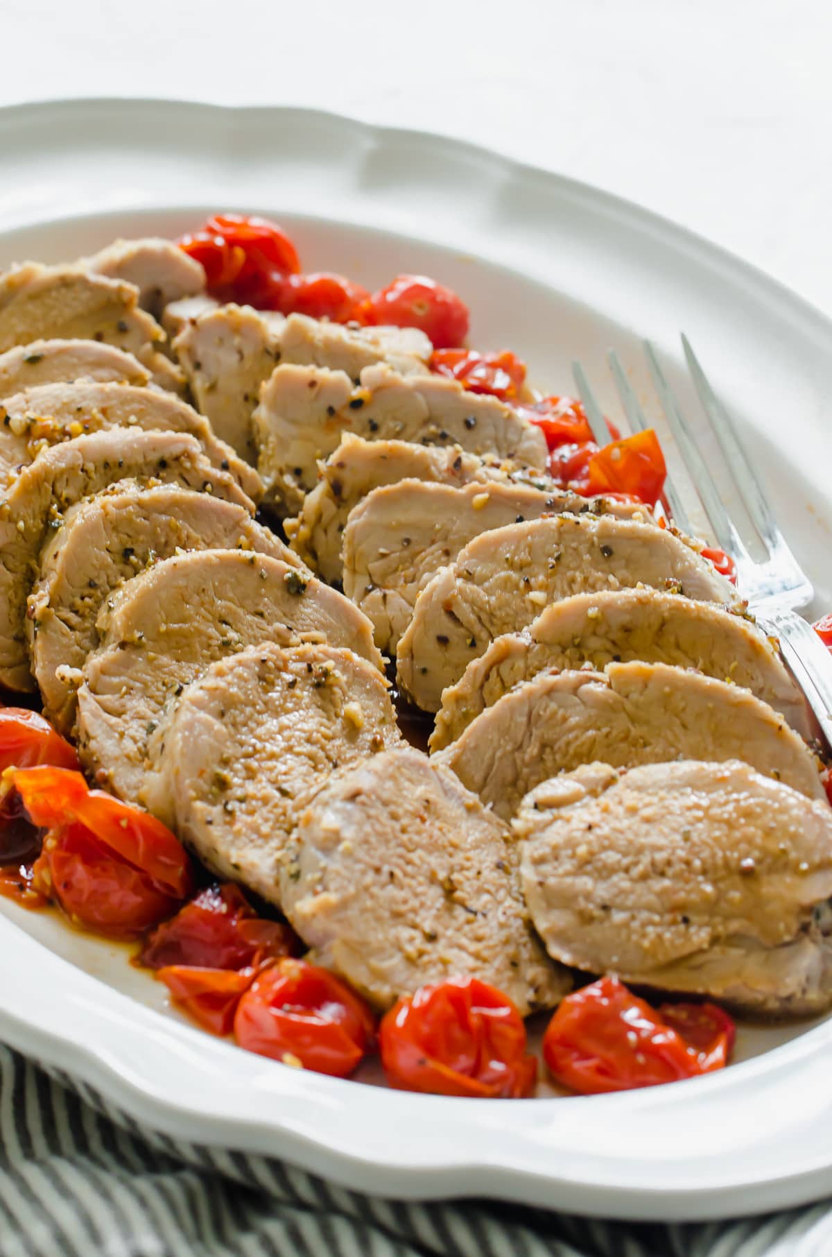 A close up shot of sliced pork with roasted tomatoes.