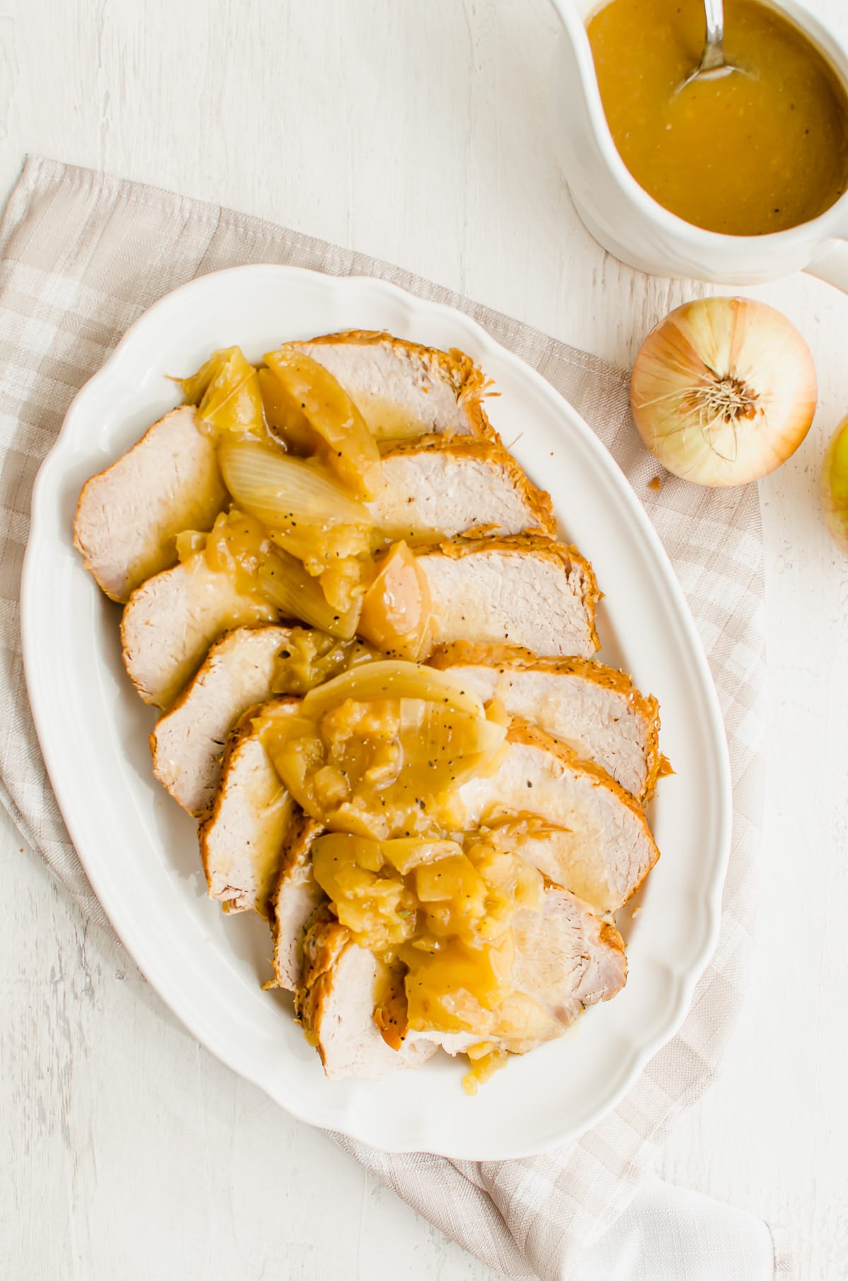 Overhead shot of a white platter with pork loin roast topped with apples, onions, and gravy.