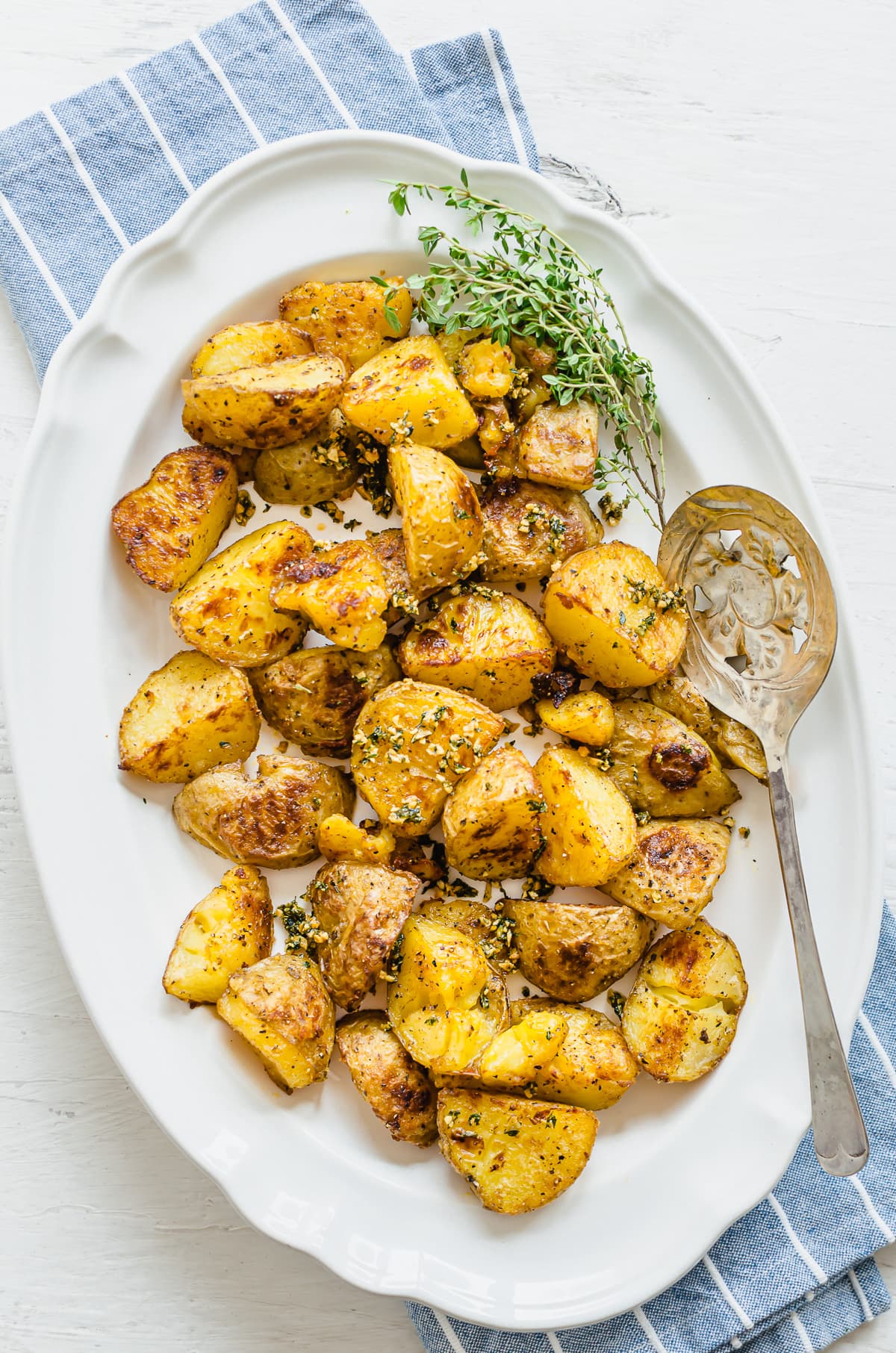 Plated crispy roasted potatoes with a serving spoon and sprig of thyme on the side.