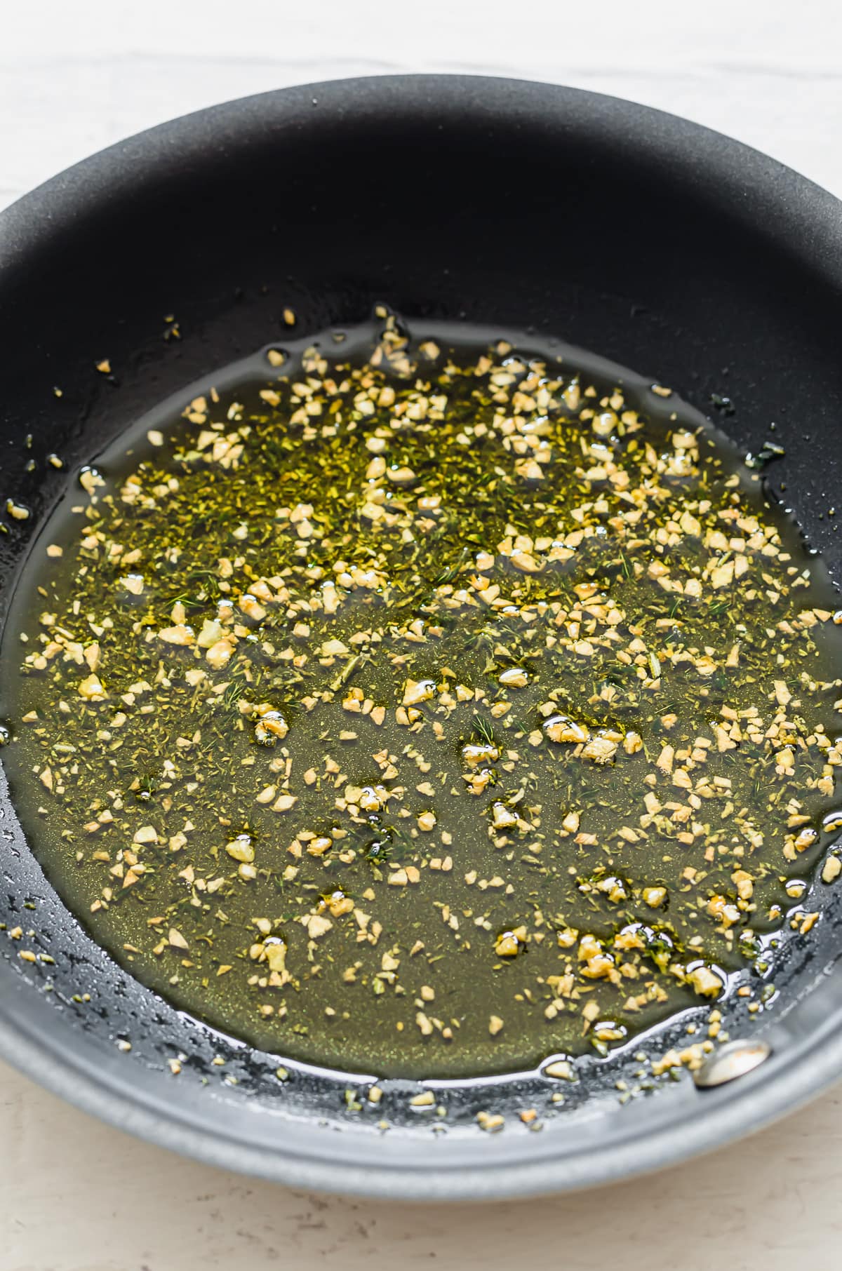 A skillet with olive oil, chopped garlic, and herbs.