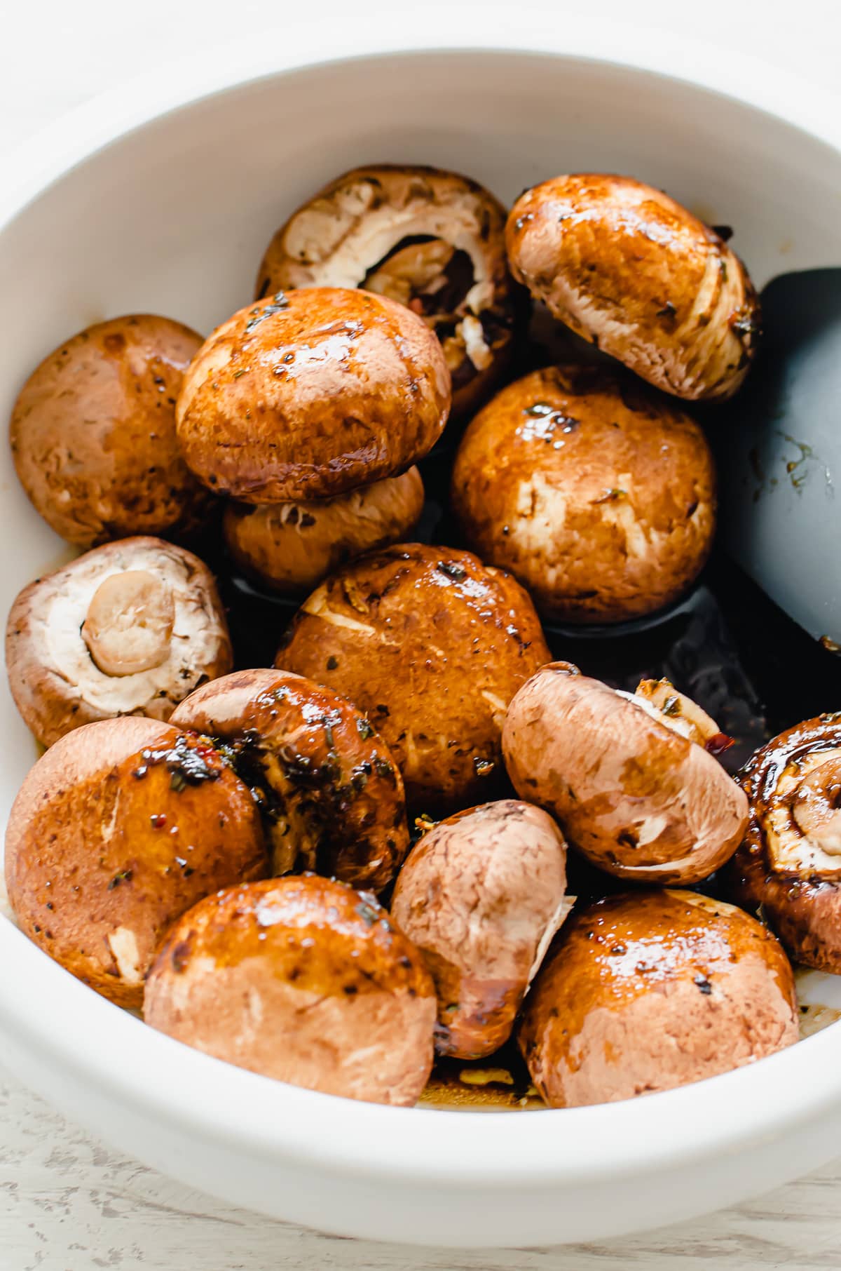 A white bowl with bella mushrooms being tossed in a balsamic sauce.