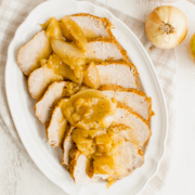 A white platter with slices of pork loin topped with apples, onions, and gravy.