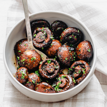 A white ceramic bowl filled with roasted mushrooms garnished with chopped parsley.