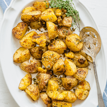 Roasted potatoes on a white platter garnished with chopped garlic and herbs.