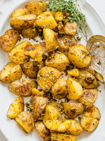 Roasted potatoes on a white platter garnished with chopped garlic and herbs.