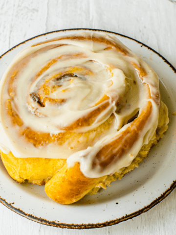 A cinnamon roll on a white rimmed plate.