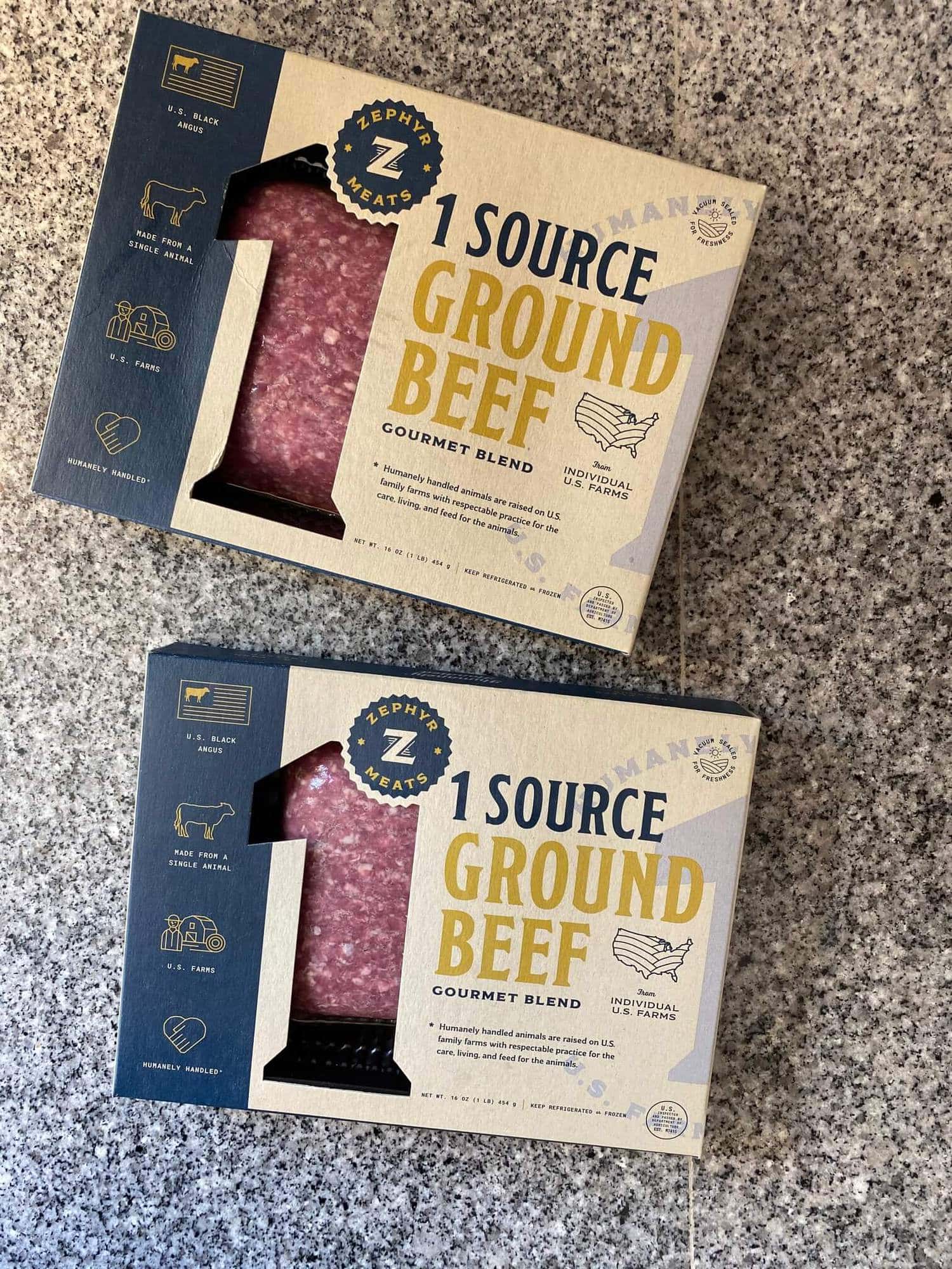 Two packages of 1 Source Ground Beef on a blue granite countertop.