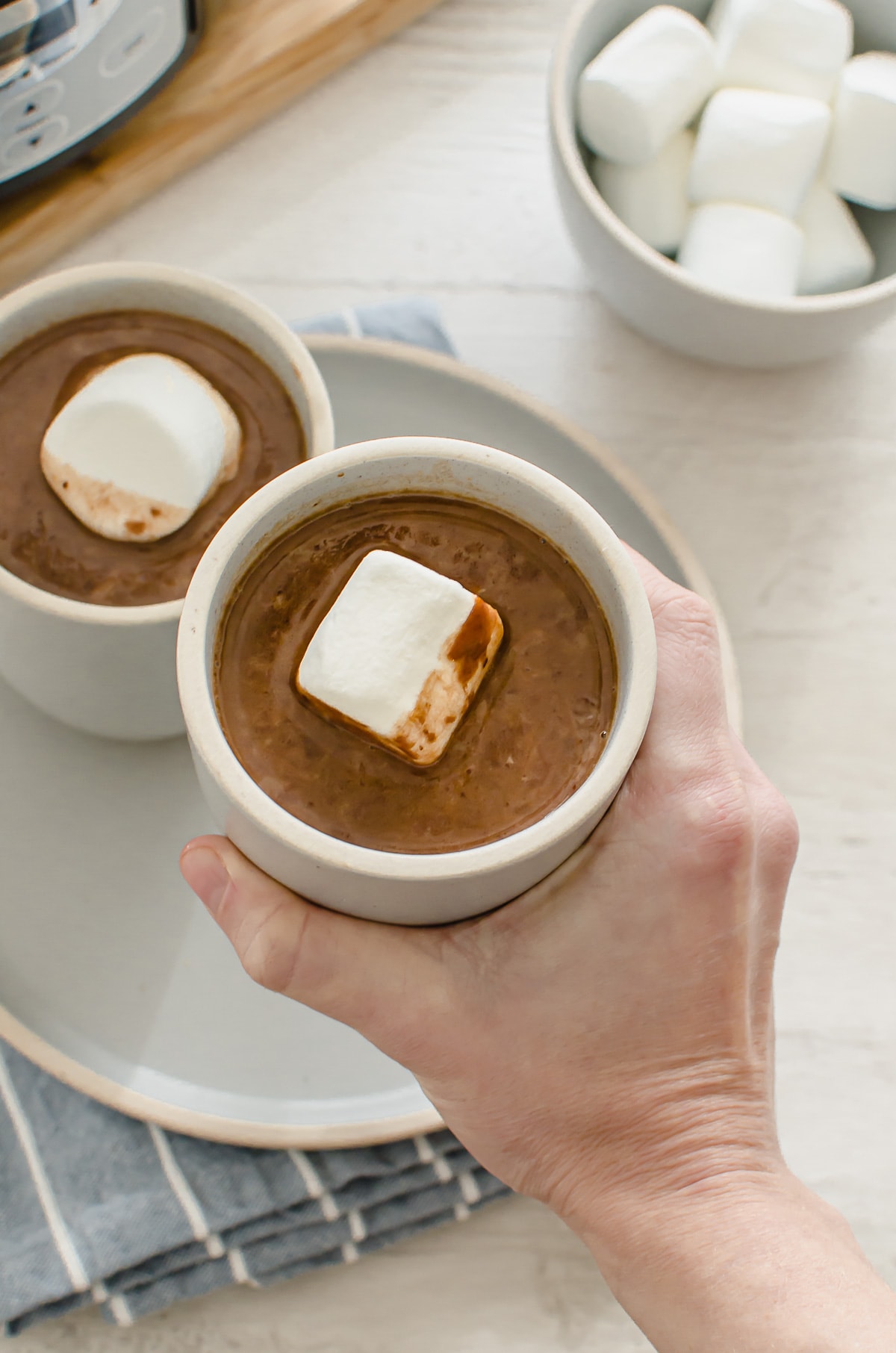 A hand holding up a cup of hot chocolate in a blue ceramic cup.