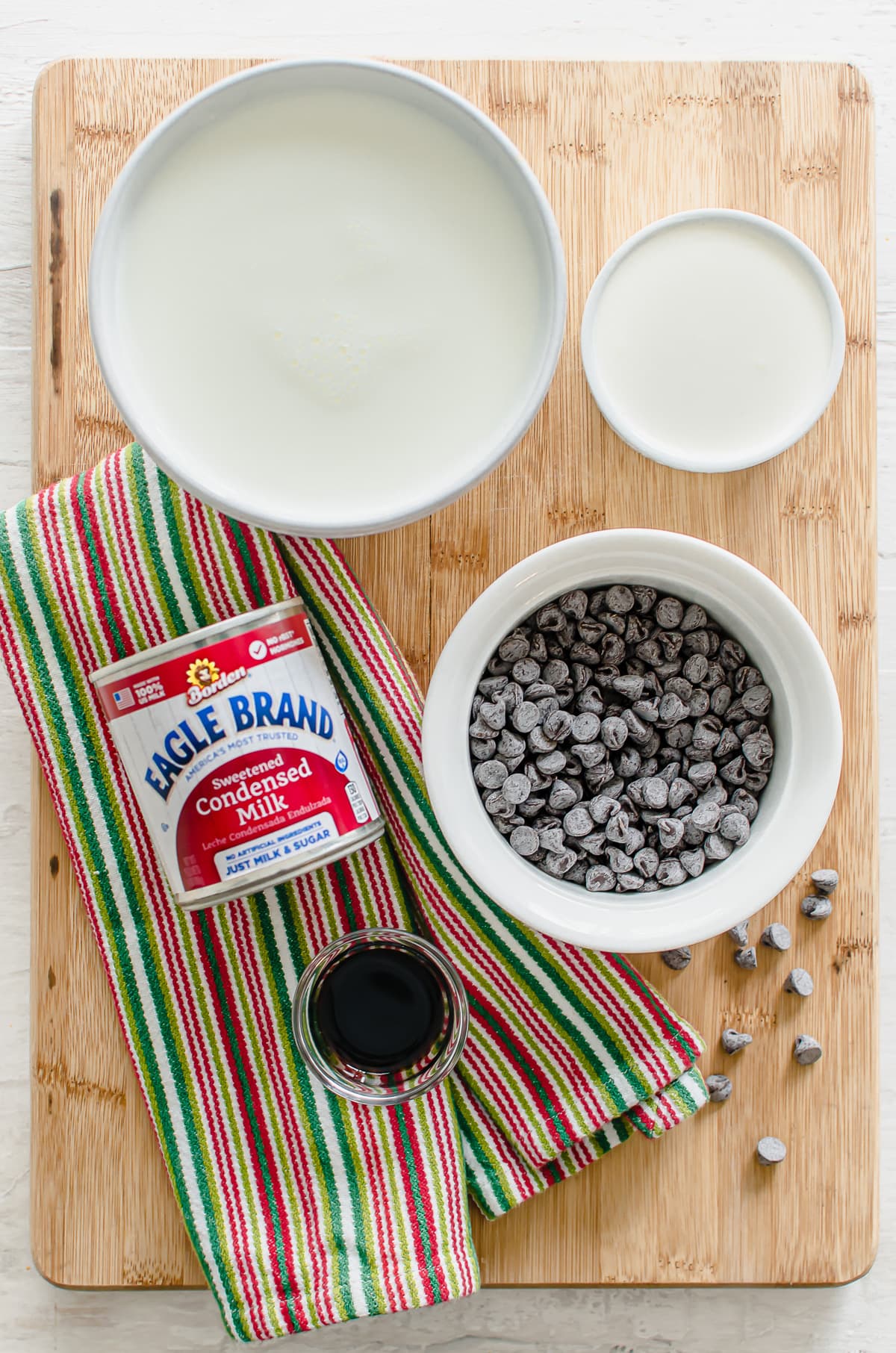 Ingredients measured out in white bowls for making slow cooker hot chocolate, including milk, cream, chocolate chips, vanilla, and sweetened condensed milk.