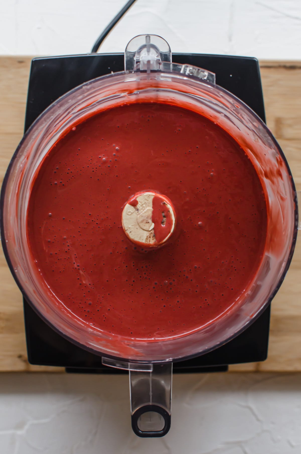Red velvet cheesecake batter in the bowl of a food processor.