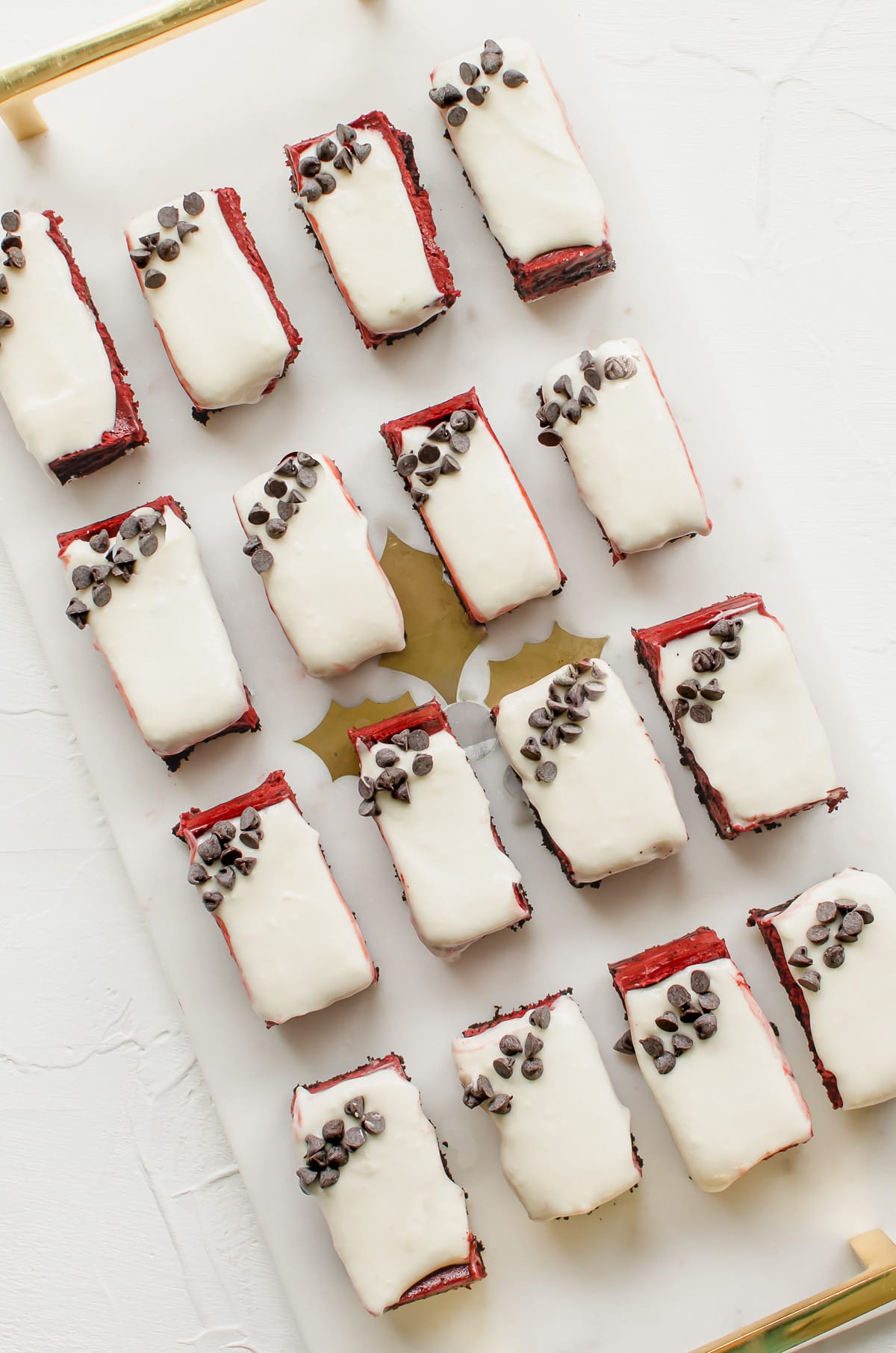 A marble platter with gold handles with red velvet cheesecake bars in rows.
