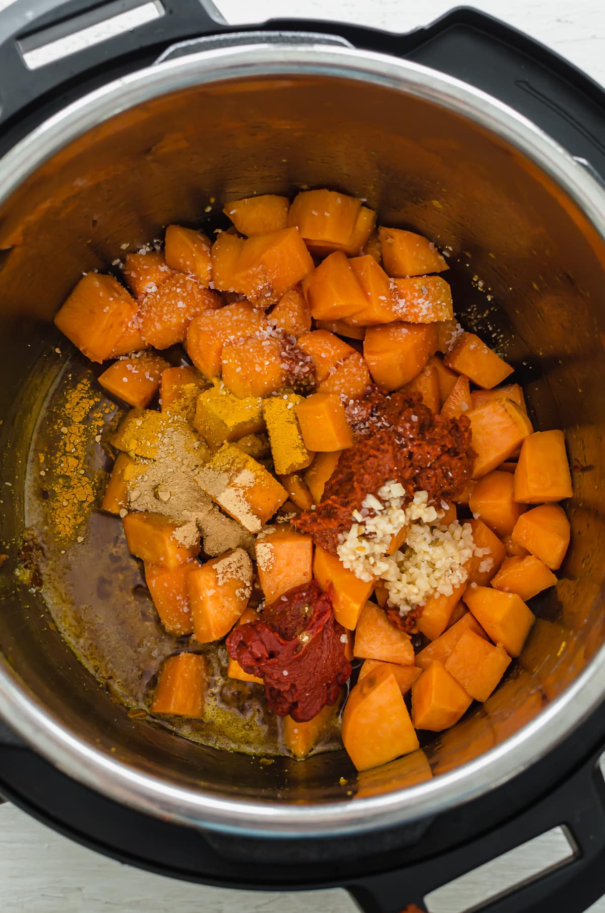 Spices and curry paste being stirred into sauteed sweet potatoes for lentil curry.