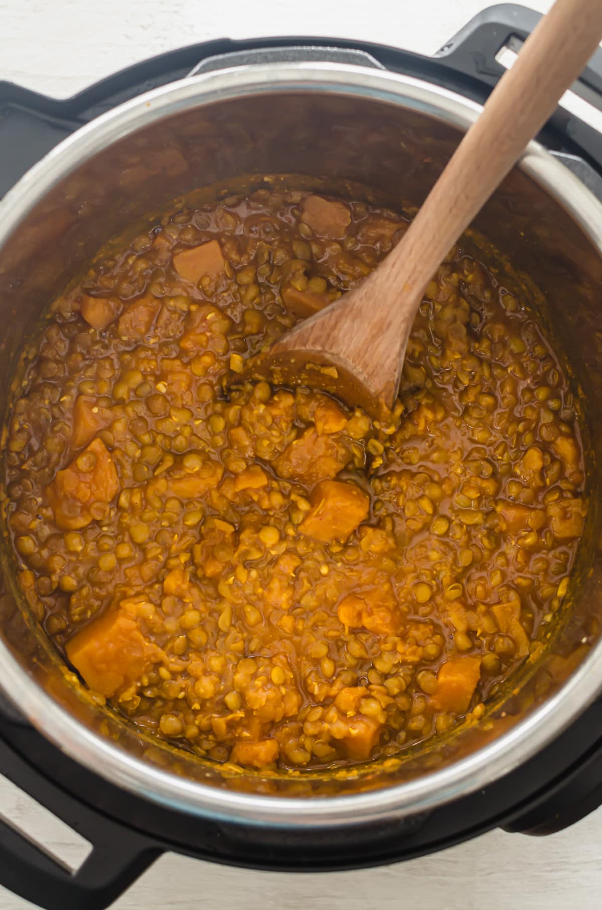 Cooked sweet potato lentil curry in an Instant Pot with a spoon on the side.