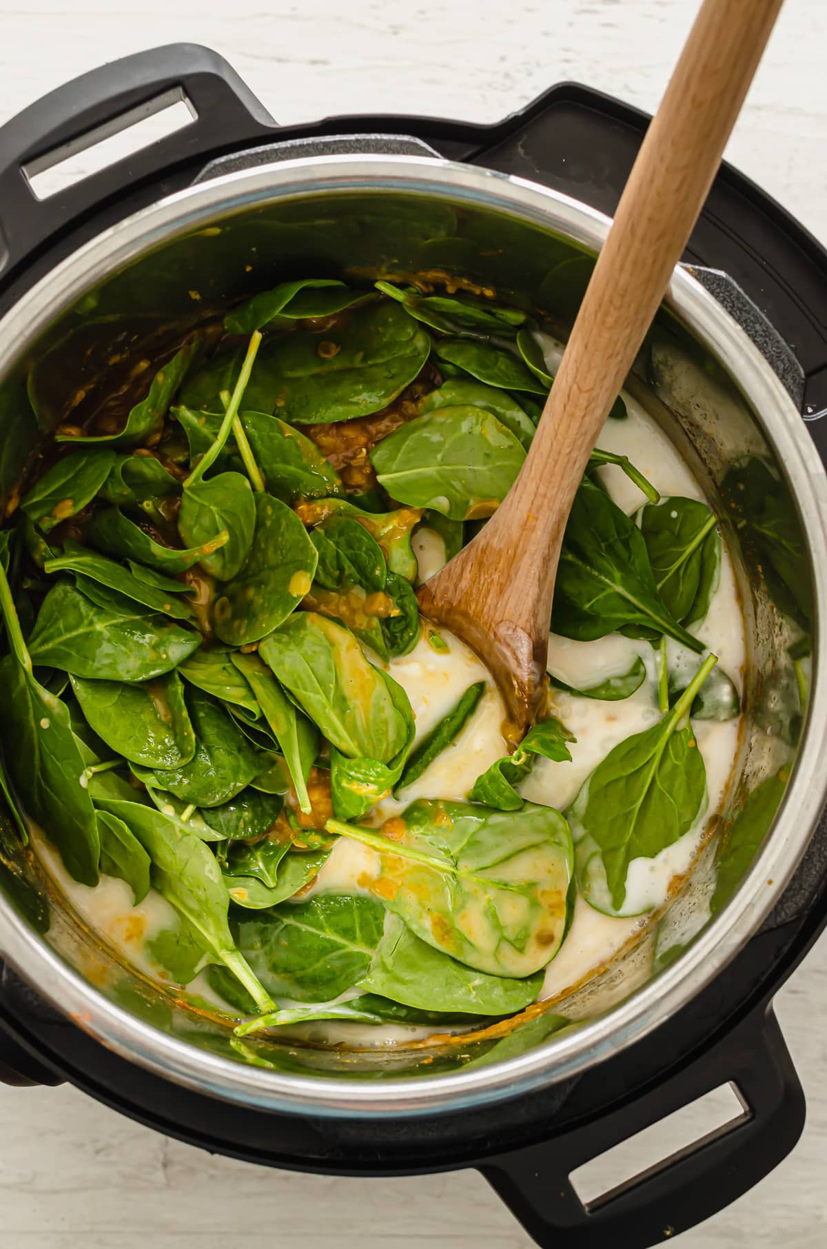 Spinach and coconut milk being stirred into an Instant Pot full of lentil curry.